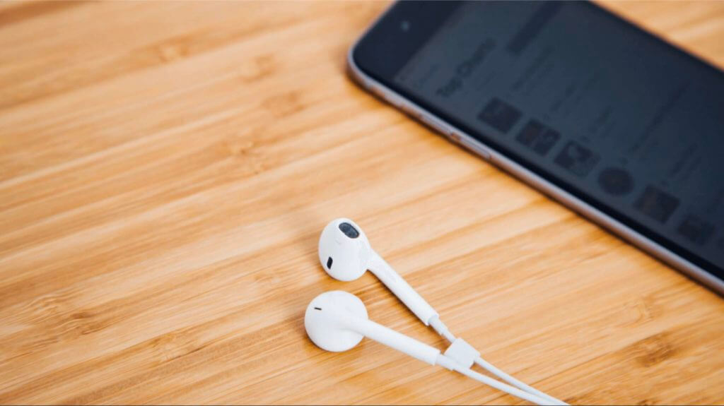 Headphones next to an iPhone with Apple Podcast Cover arts on the screen
